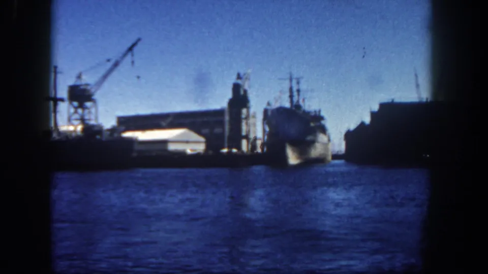 1962 San Diego waterfront view with a docked naval ship, industrial pier equipment, warehouses, and blue water.