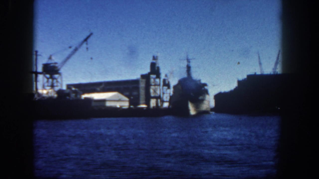 Harbor water with docked industrial ships, cranes, and dark film-frame borders.