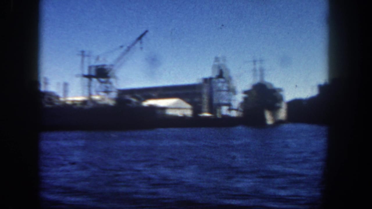 Industrial waterfront with a large docked vessel, crane, and harbor water.