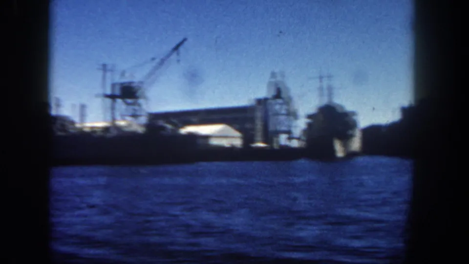 San Diego harbor waterfront in 1962, showing a large docked vessel, crane silhouettes, and blue water through dark 8mm frame edges.