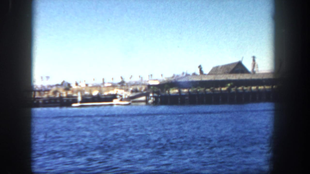 Harbor water with a long pier and roofed building seen through dark film frame edges.