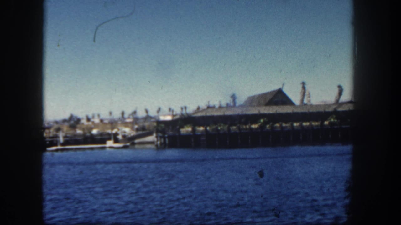 Long waterfront pier and roofed building across blue harbor water.