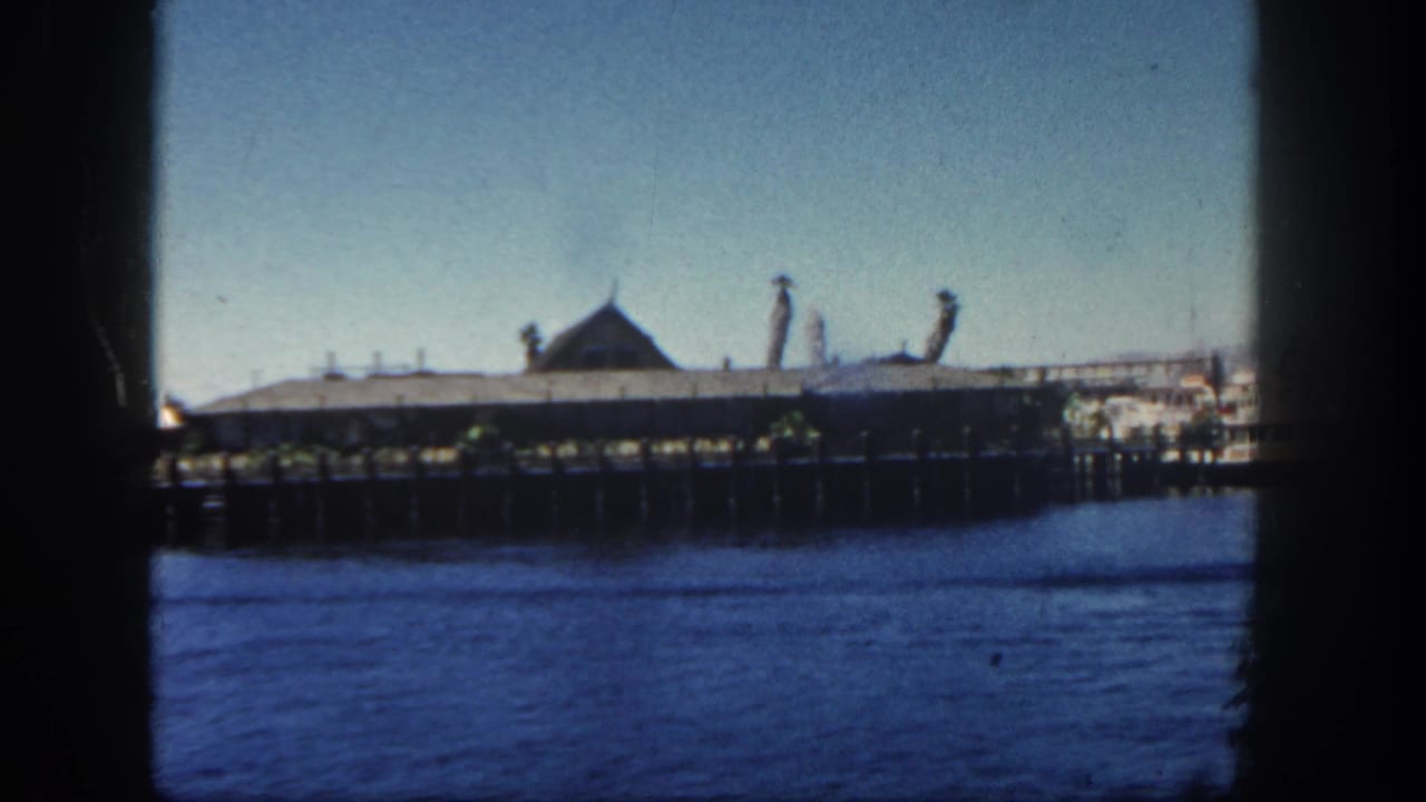San Diego waterfront pier building in 1962, framed by dark 8mm edges with blue water in the foreground and a clear sky above.