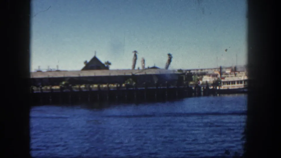 A 1962 San Diego harbor view shows the pier building across blue water, with a small vessel or docked boat appearing near the right edge.