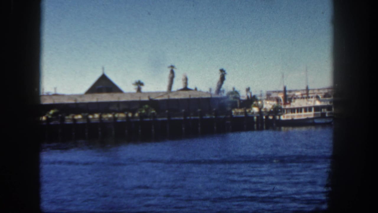 Pier over blue water with pointed-roof building and docked white boat at right.