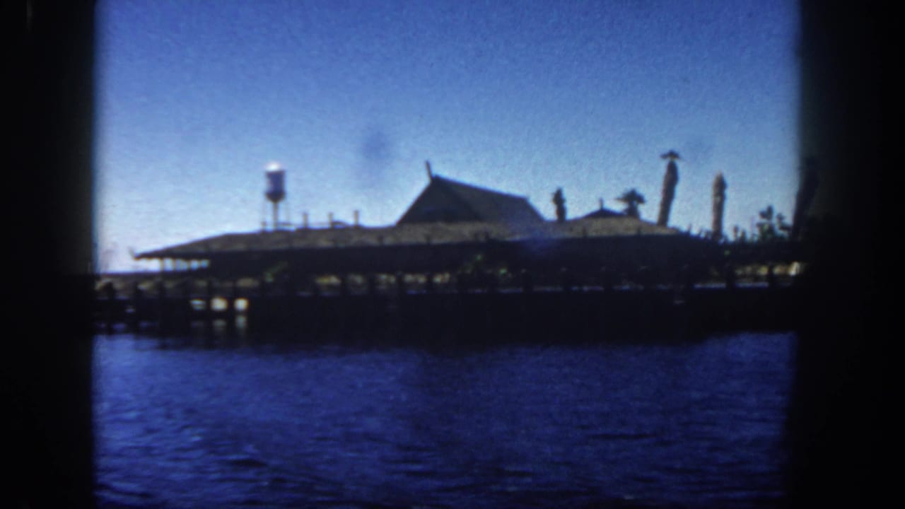 San Diego pier scene from 1962 showing a low waterfront structure, small water tower, and dark blue harbor water.