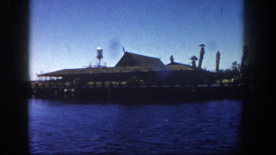 Vintage 8mm San Diego harbor view with the pier, water tower, pointed-roof building, and decorative vertical poles.