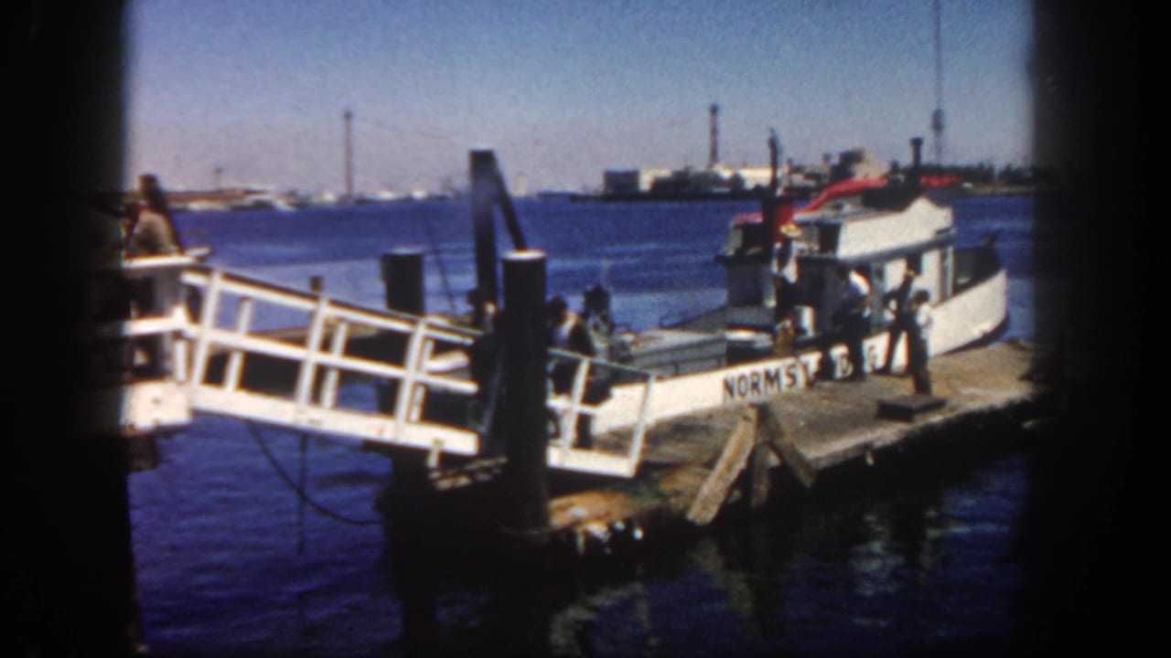 Small white boat beside a wooden pier with men near a boarding ramp.