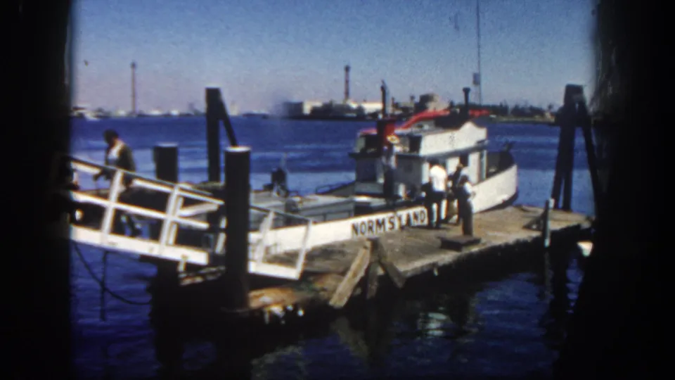 Home-movie view of a small boat at a wooden San Diego harbor pier, with men beside the ramp and visible film edge shadowing.