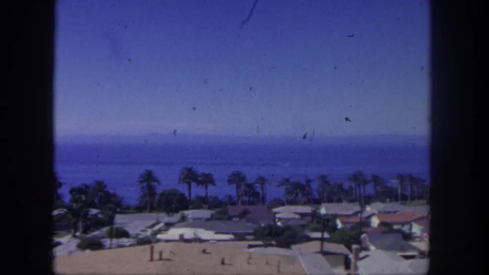 Elevated 1962 San Pedro view across a low coastal neighborhood, palm trees, and the Pacific horizon on faded 8mm film.