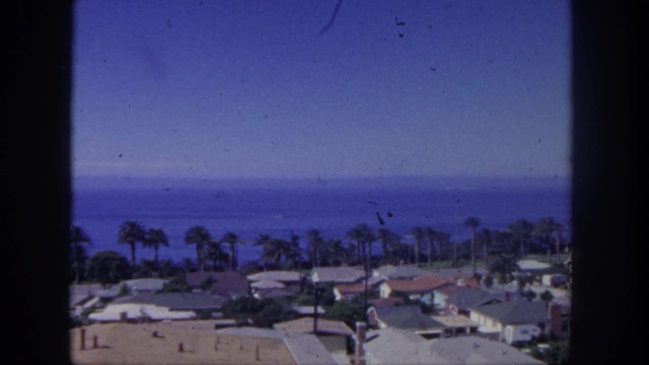 San Pedro coastal home-movie frame with palm trees, houses, and a blue ocean horizon, bordered by the 8mm film frame.