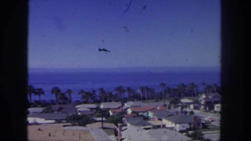 Elevated 1962 San Pedro view of coastal palms, low homes, and ocean, with dust and scratches visible in the 8mm scan.
