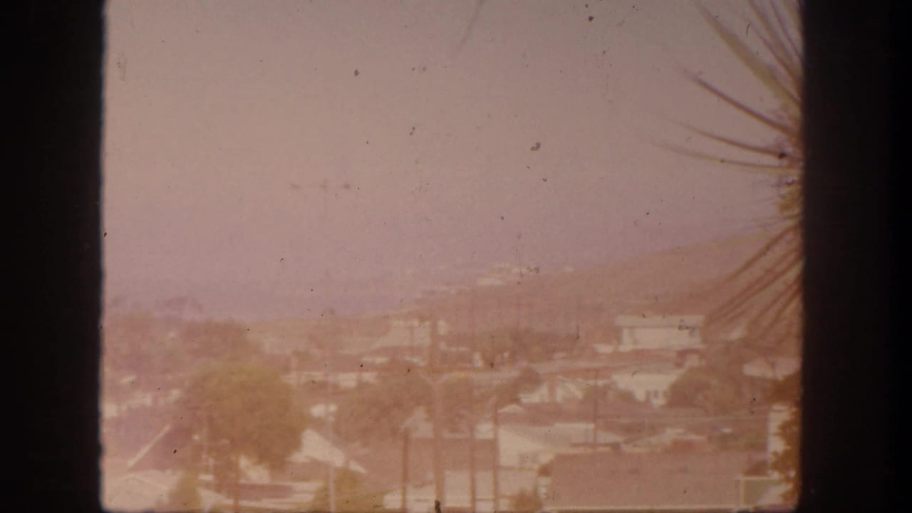 San Pedro, California rooftops and distant hills appear through a window frame in soft, faded 8mm color.