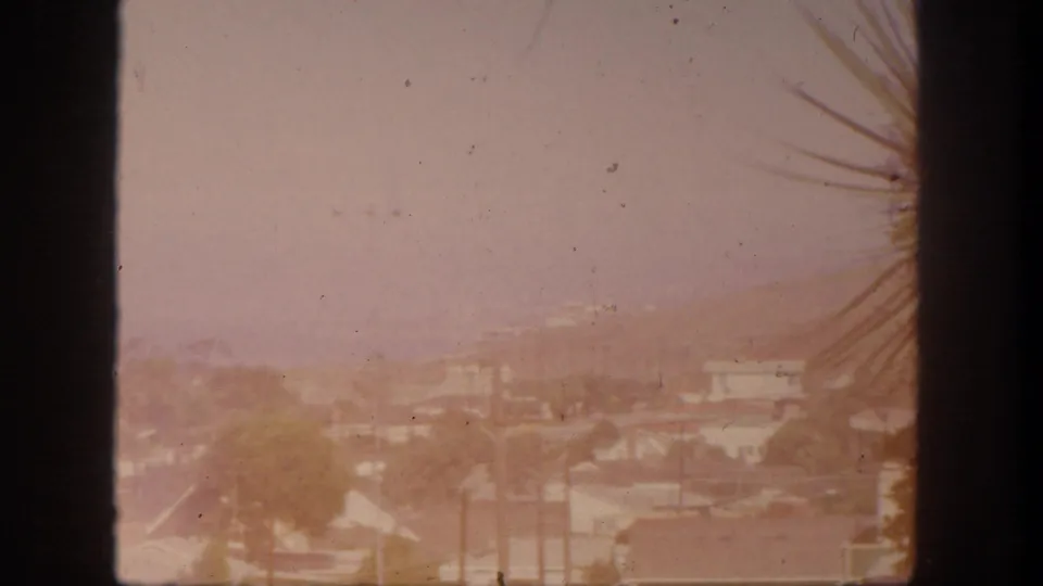 San Pedro, California rooftops and distant hills appear through a window frame in soft, faded 8mm color.