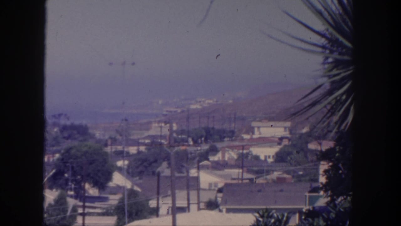 Elevated view over houses and utility poles toward distant water, partly framed by a dark foreground edge.