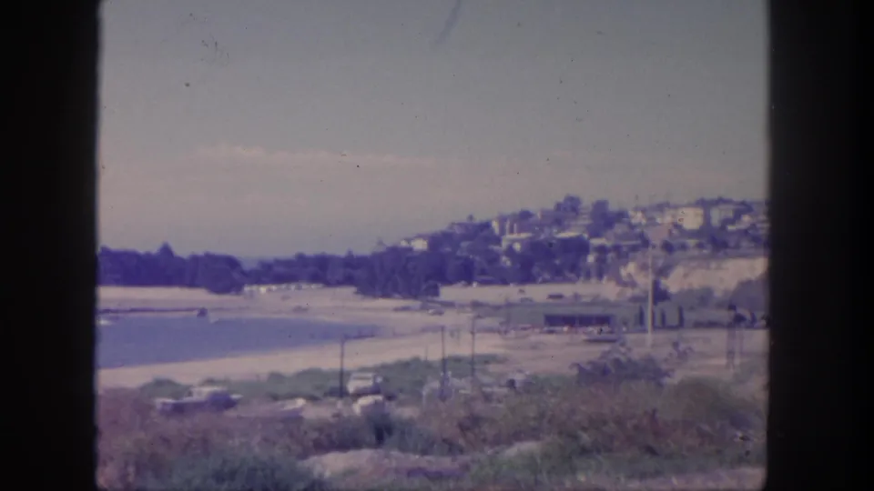 1962 San Pedro coastal view with beach, water, hillside residences, roadside cars, and dark foreground framing.
