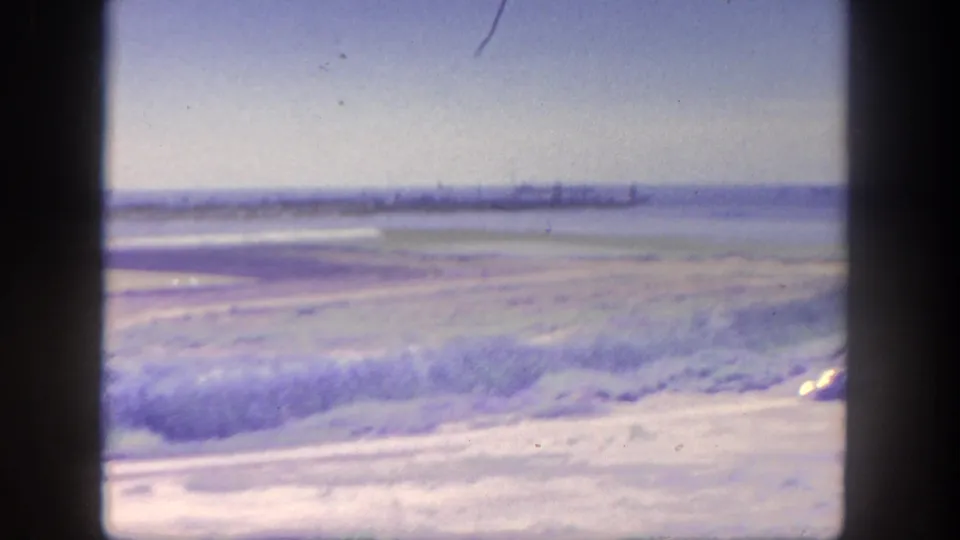 Overexposed 1962 San Pedro harbor frame with bright dry foreground, water, faint distant port structures, and dark 8mm frame borders.