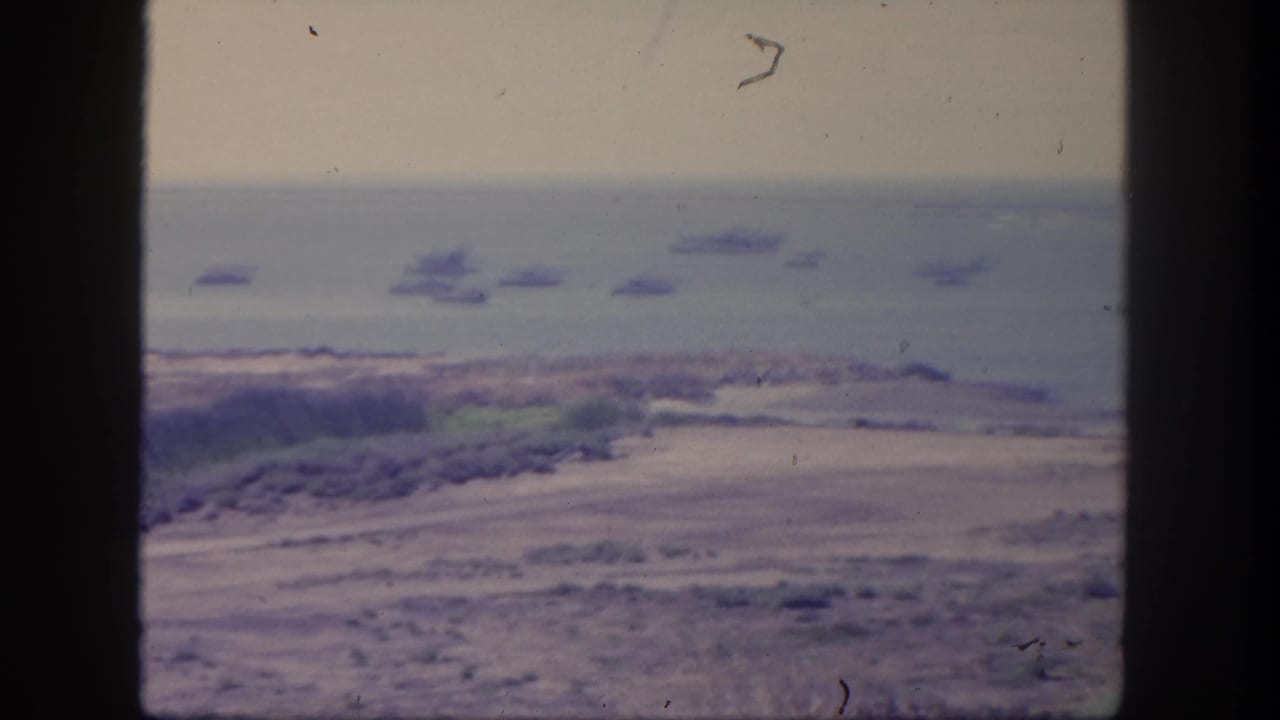 Hazy coastal overlook with anchored ships offshore and shoreline below.