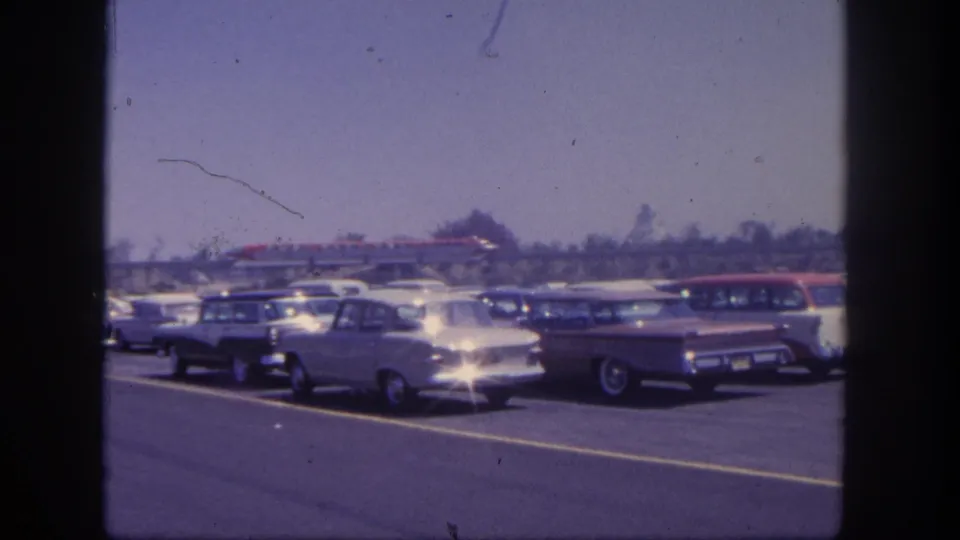 1962 San Pedro parking area with sedans and station wagons, plus a distant rail feature crossing the background.