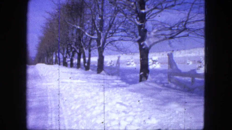 1963 Proctor, Minnesota home-movie frame showing a snow-covered road, bare trees, deep banks, and a low fence.