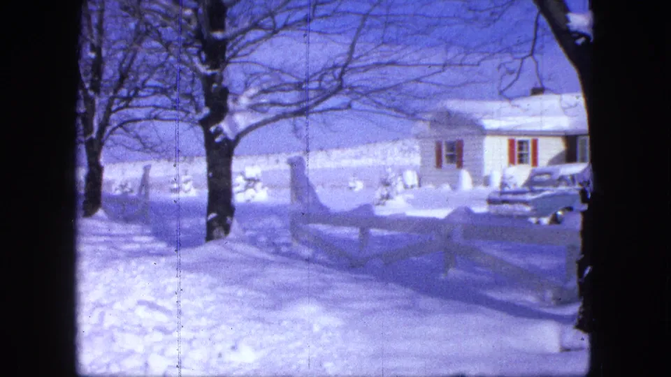 1963 Proctor, Minnesota frame showing a white house with red shutters, a parked vehicle, deep snow, trees, and a fence.