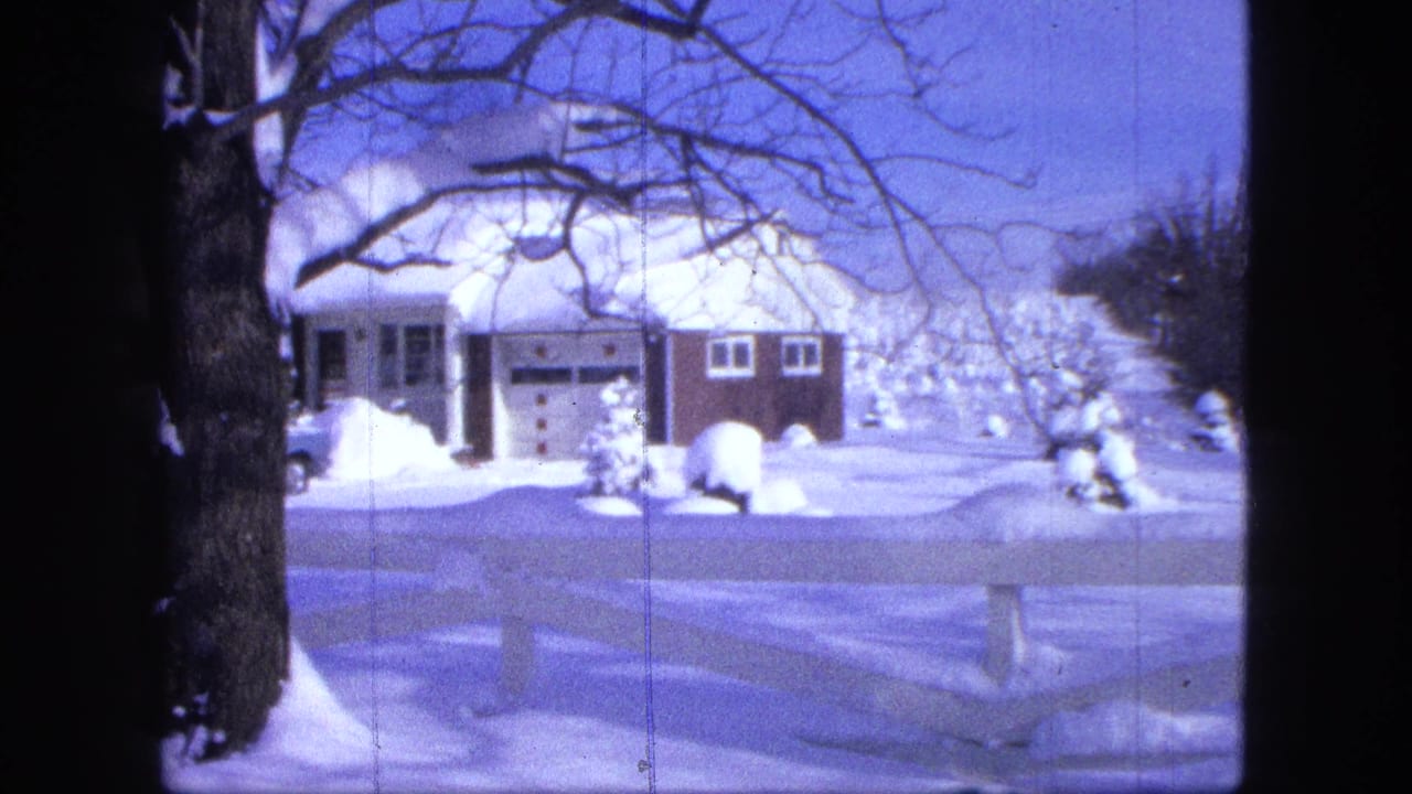 1963 Proctor, Minnesota home-movie frame of a snow-covered suburban house and white fence under bare winter branches.