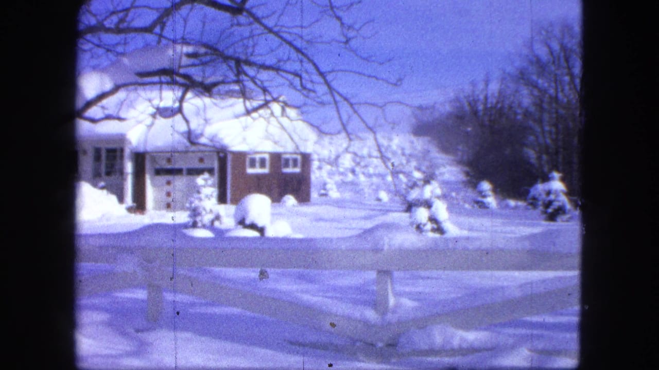 Snow-covered Proctor house in a 1963 8mm frame, with dark vertical edges and bare branches framing the winter view.