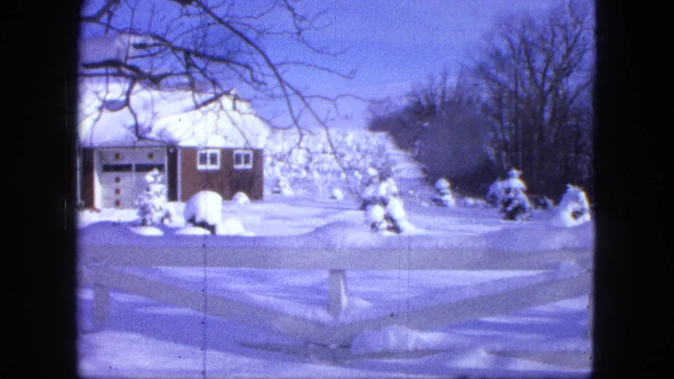 1963 Proctor, Minnesota frame showing a snowy suburban house, garage, fence, and leafless trees in a deep winter yard.