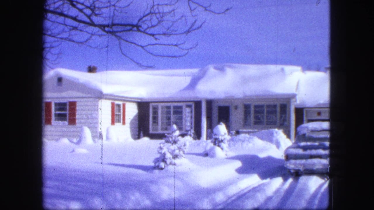1963 Proctor, Minnesota frame of a snow-buried residential exterior with a white house, red shutters, and a car partly visible at right.