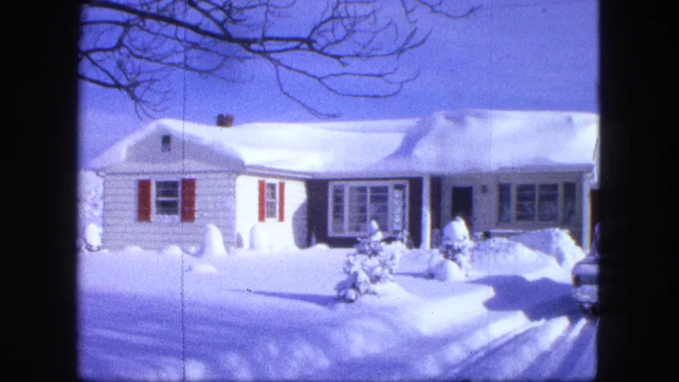 1963 Proctor, Minnesota 8mm frame showing the front of a white residential house, red shutters, and piled snow across the yard.