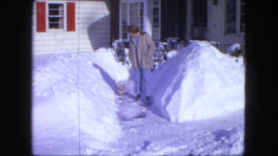 1963 Proctor, Minnesota home-movie frame of a woman with a small dog on a shoveled residential path in deep snow.