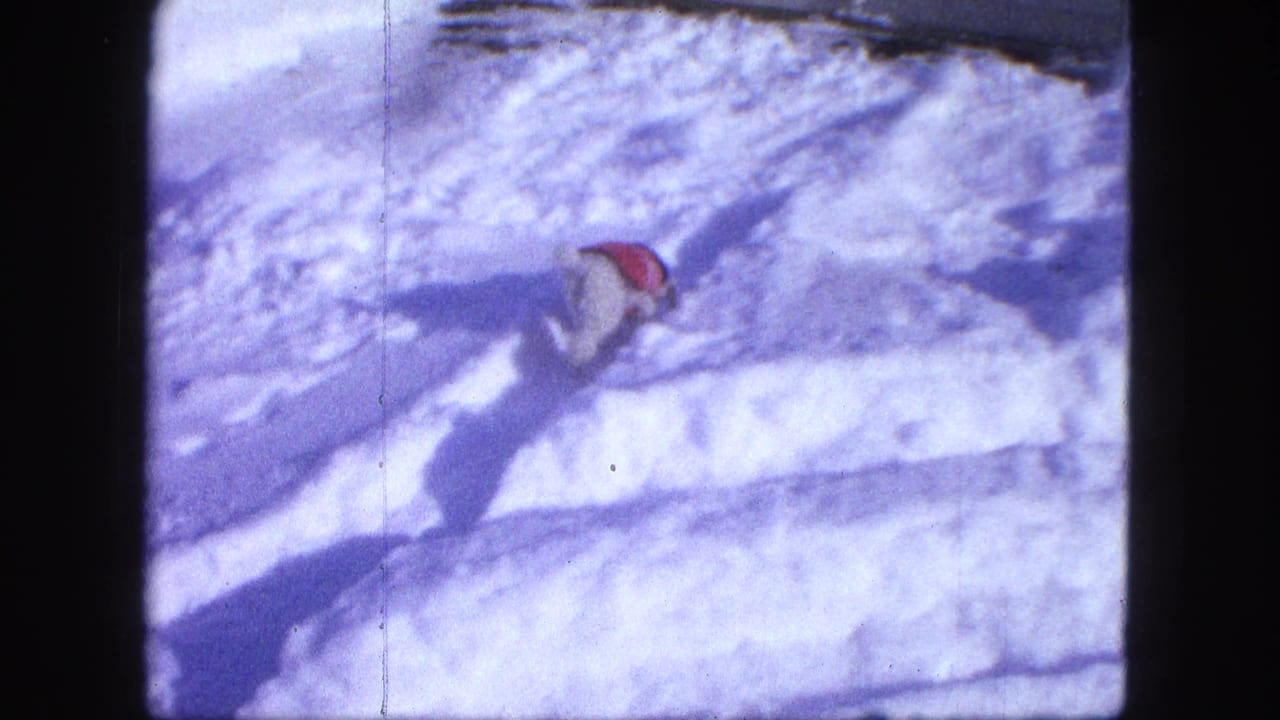Dog in a red coat climbing over a snowy ridge near tire tracks.