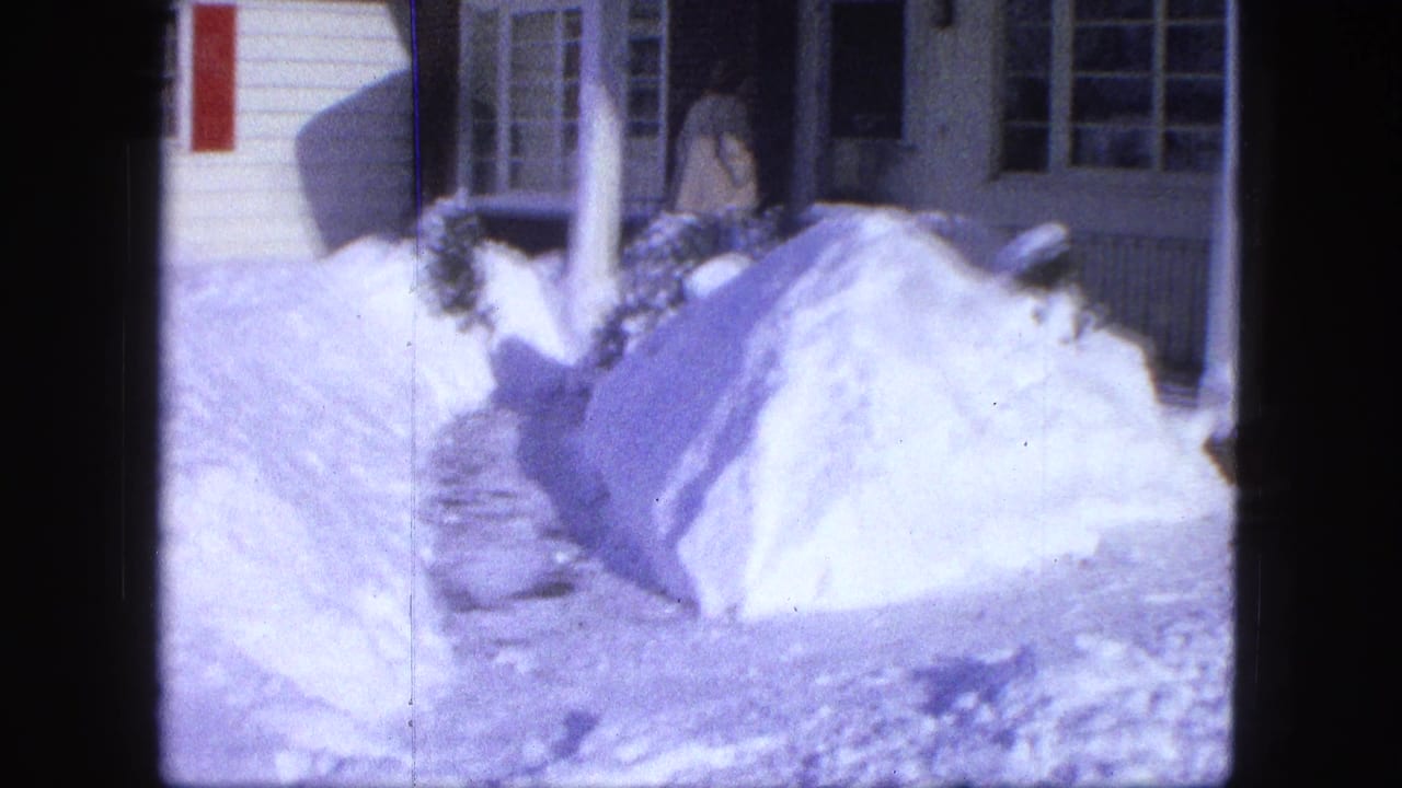 Person near a front porch with deep snowbanks beside a cleared walkway.