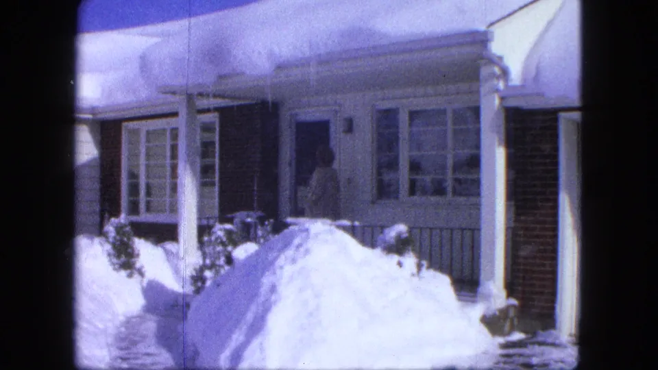 A bundled figure enters the front door of a snow-covered Proctor, Minnesota house in this 1963 8mm home-movie frame.