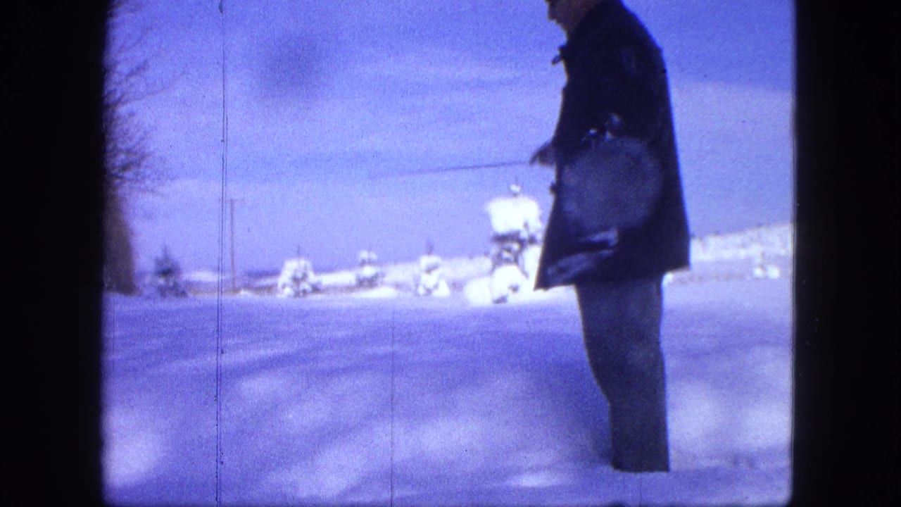 Man stands in deep snow holding a bag and a long pole.