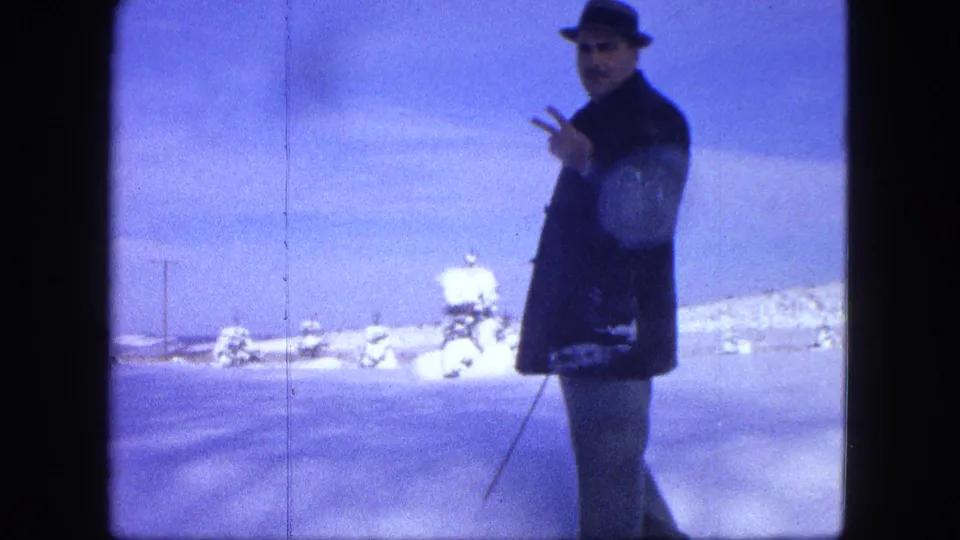 The man remains in the snowy Proctor, Minnesota landscape, holding a pole and gesturing toward the home-movie camera.