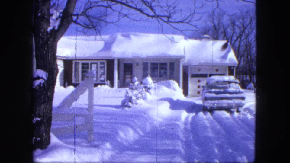 8mm winter frame from Proctor, Minnesota, with a snow-covered residence, driveway car, fence post, and bare trees.