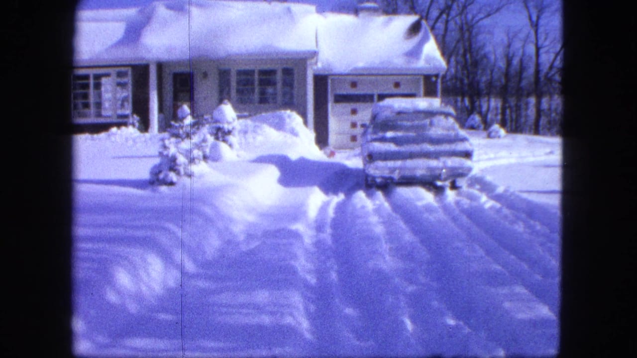 Snow-covered house with a car buried in snow at the driveway.