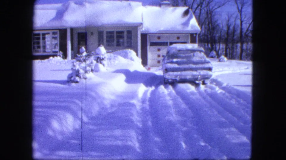 1963 Proctor, Minnesota home-movie frame showing a snowy house, garage, driveway tracks, and a car covered in deep snow.