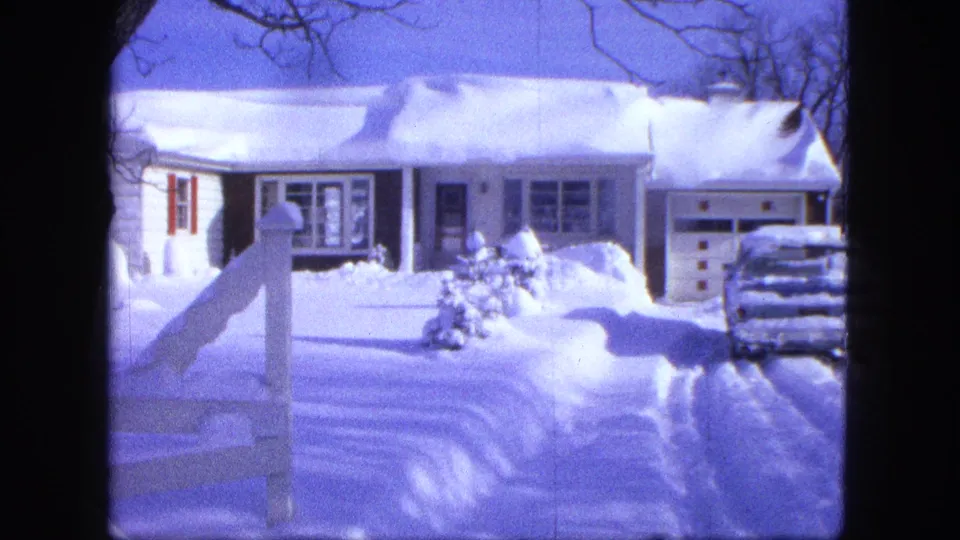 A wider home-movie view shows the snowbound Proctor residence, partial fence, driveway tracks, and car beside the garage.