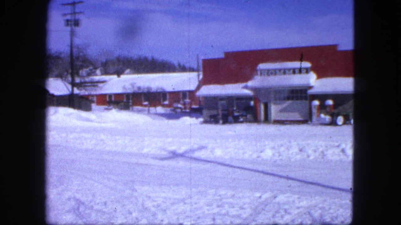 Snowy street facing a red commercial building with a HOMMER sign and parked vehicles.