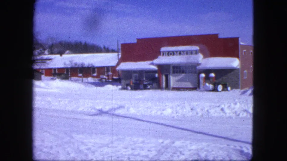1963 Proctor, Minnesota frame showing a red commercial building with HOMMER signage, snowbanks, and parked cars.