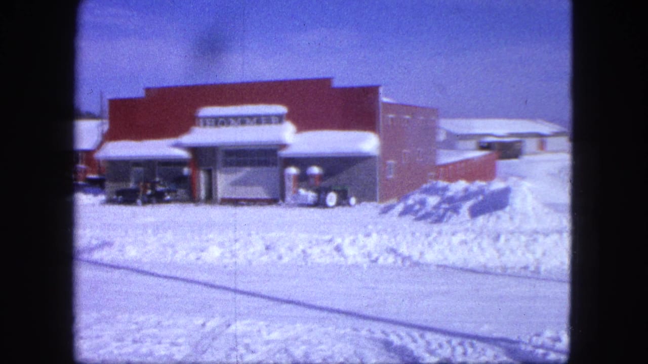 1963 Proctor, Minnesota 8mm frame showing a snowy roadside view of a red brick building with a HOMMER sign and parked cars.
