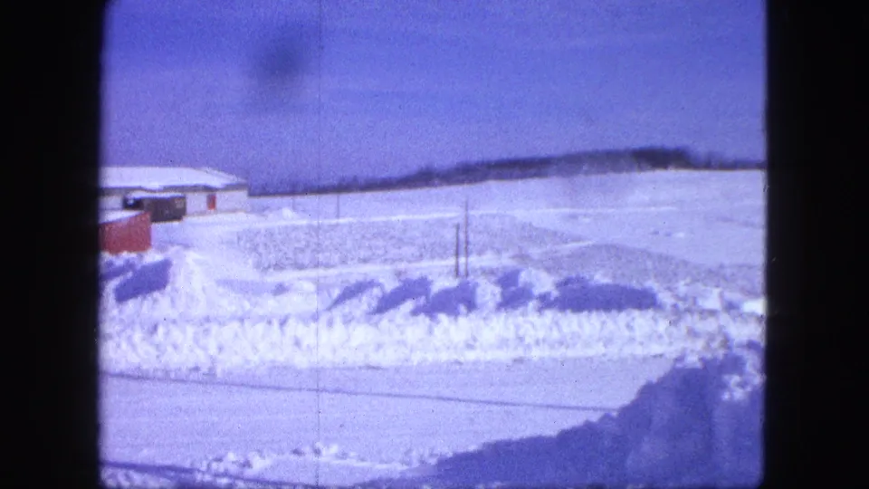 1963 Proctor, Minnesota 8mm view across a snowy roadside toward an open field and low white-roofed building.
