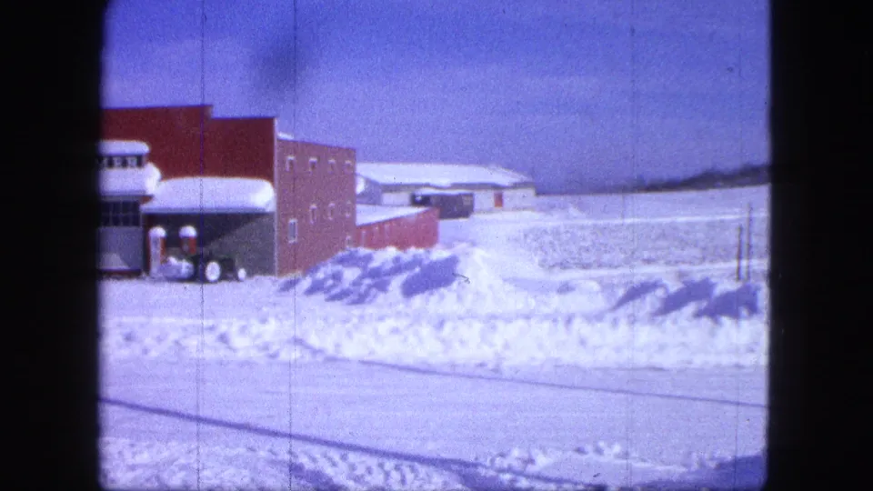 1963 Proctor, Minnesota frame with the HOMMER storefront sign, deep snowbanks, and a plow-equipped vehicle positioned by the building.