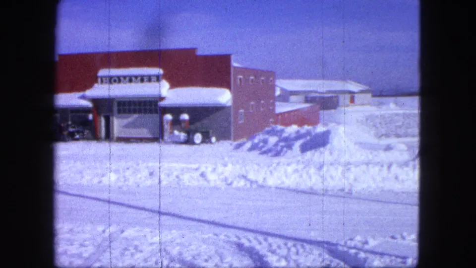 1963 Proctor, Minnesota home-movie still showing a plow-equipped Jeep by the HOMMER storefront and heavy roadside snow.