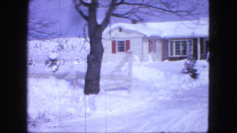 1963 Proctor, Minnesota 8mm frame showing a white house, red shutters, bare tree trunk, and snow piled along the roadside.