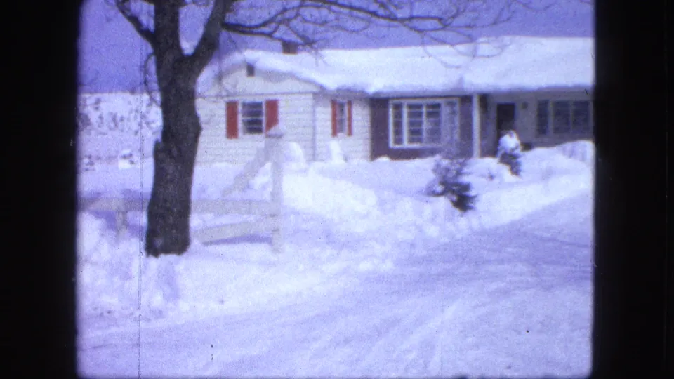 1963 Proctor, Minnesota winter frame with a snow-covered road, white house, red shutters, bare tree, and packed snowbanks.