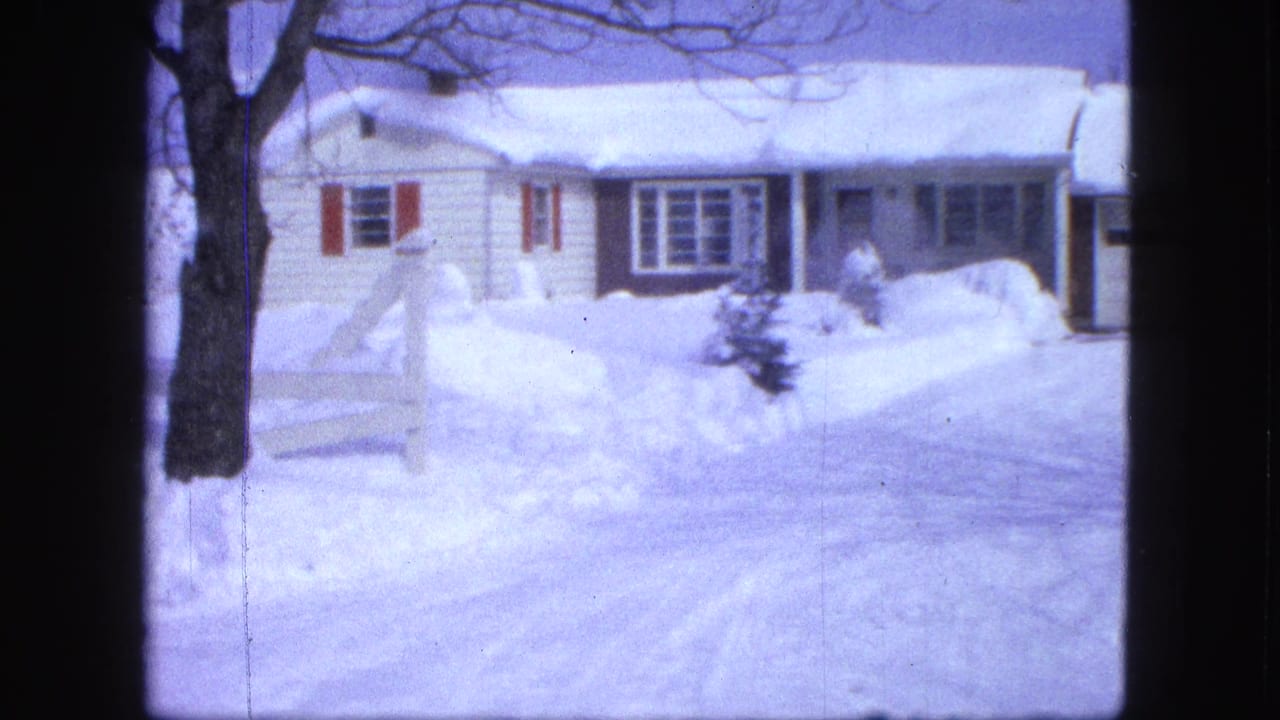 Snow-covered white house with red shutters and high snowbanks in front.