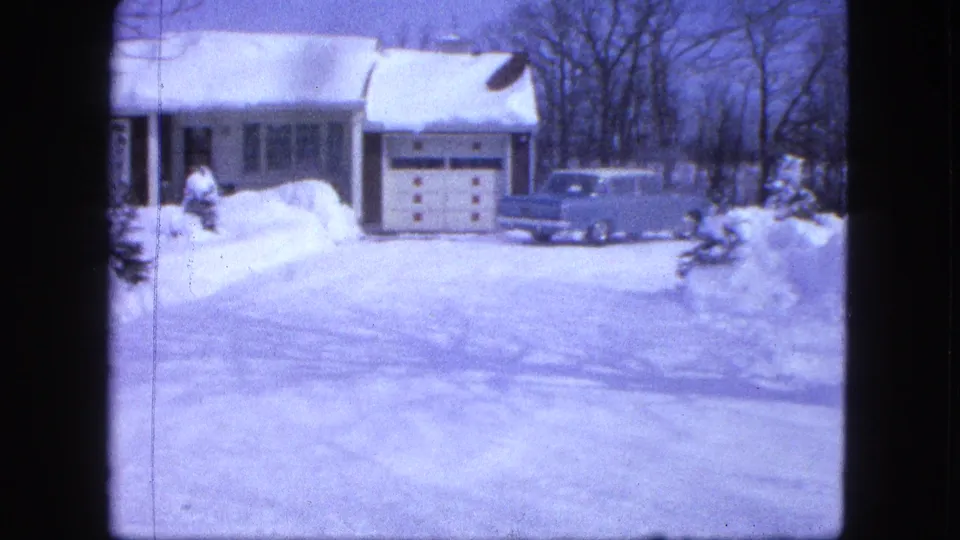 1963 Proctor, Minnesota frame with a blue car parked beside a white house and garage, surrounded by high snowbanks and bare winter trees.